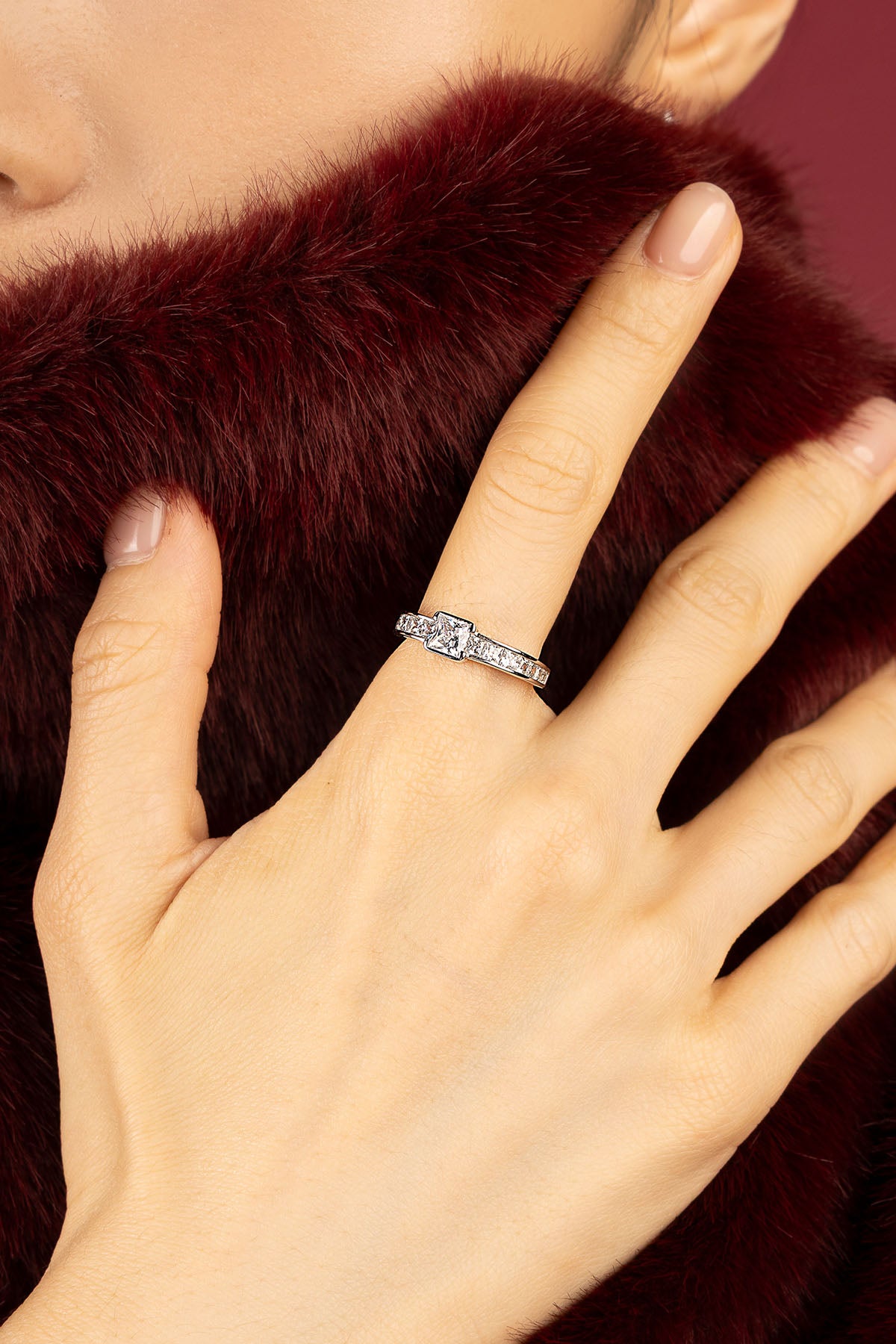 Femme portant la bague APM Monaco, éclat scintillant sur fourrure bordeaux, élégance intemporelle.