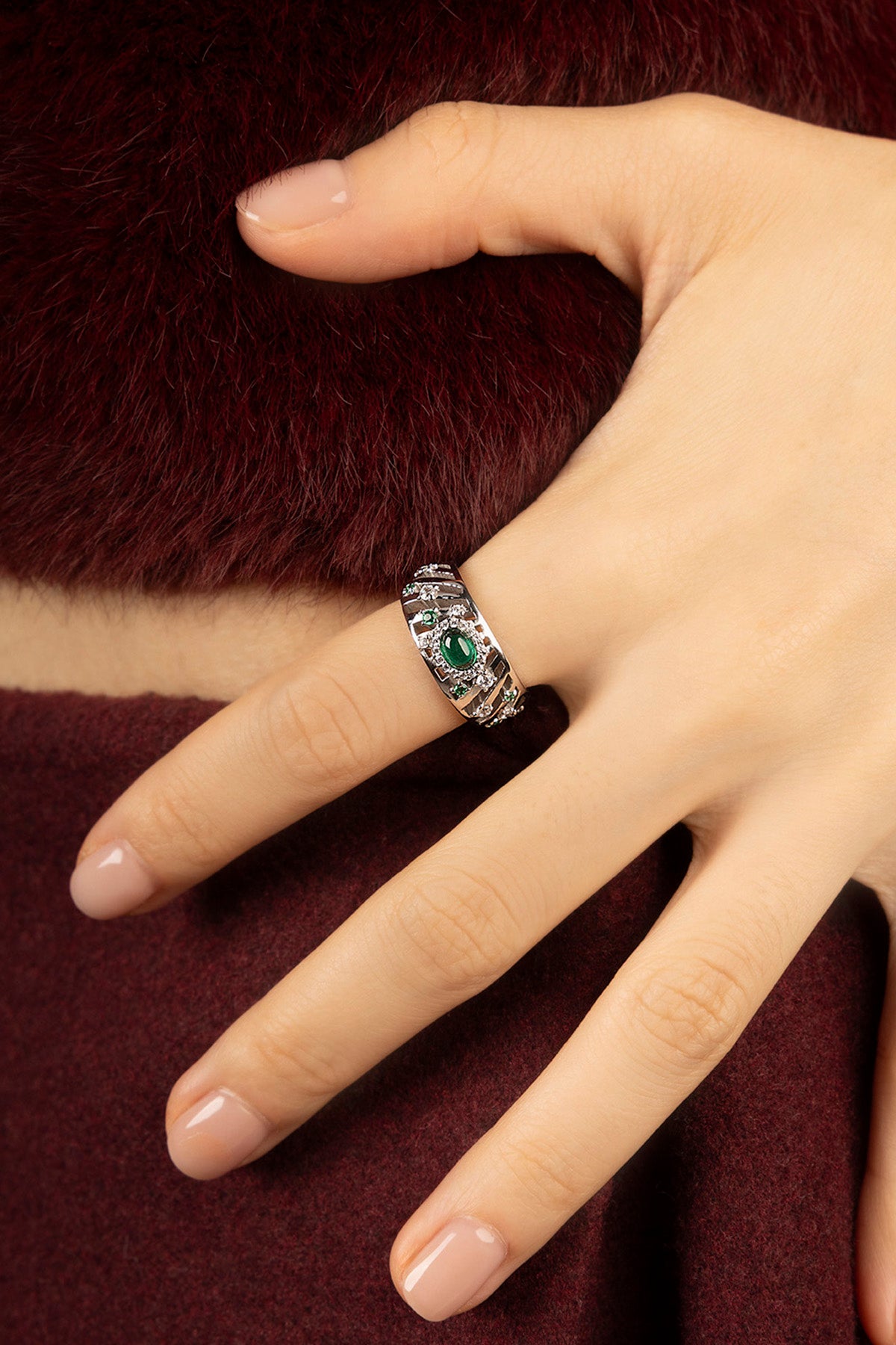 Femme portant une bague APM, éclat vert émeraude et finition rhodium, allure précieuse et intemporelle.