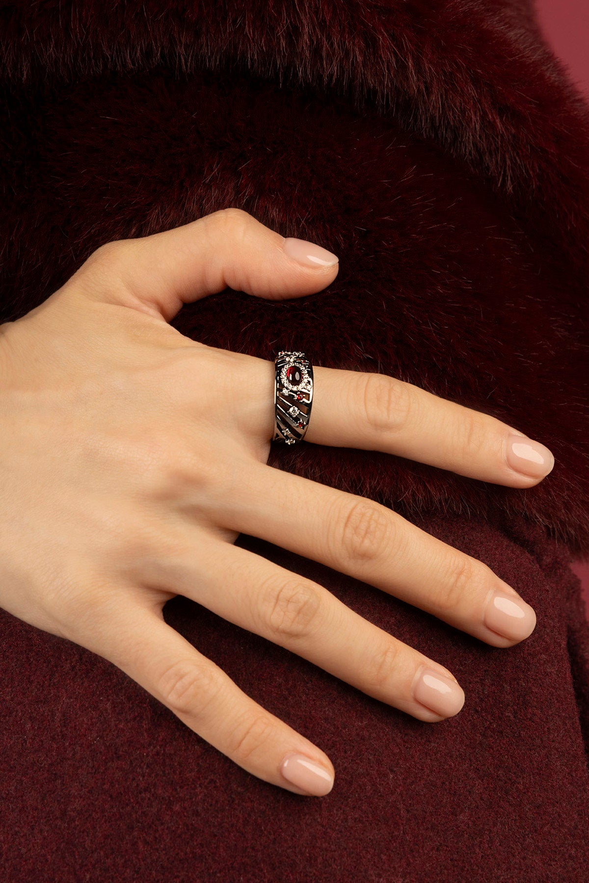 Femme portant la Bague APM Monaco, éclat rouge sur fourrure bordeaux, élégance hivernale assumée.