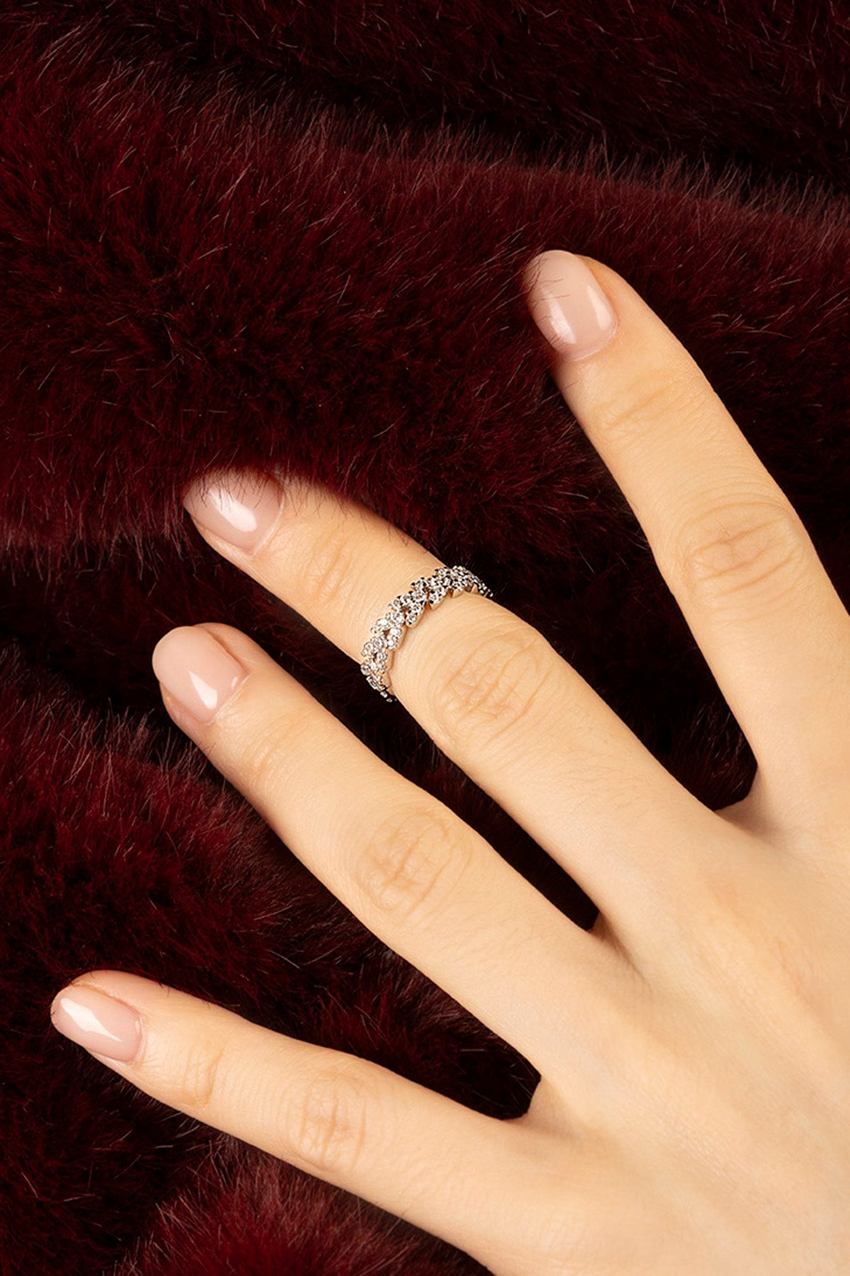 Femme portant la Bague APM, éclat scintillant sur fourrure bordeaux, élégance intemporelle.