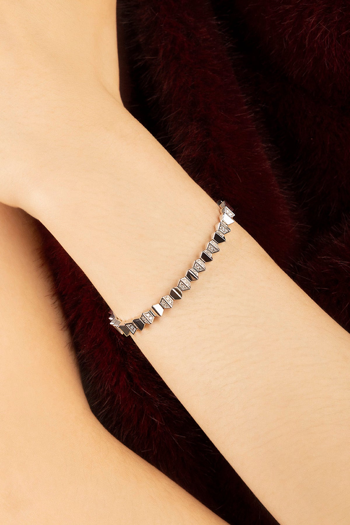 Femme portant le bracelet APM, éclat graphique et allure raffinée sur fourrure bordeaux.