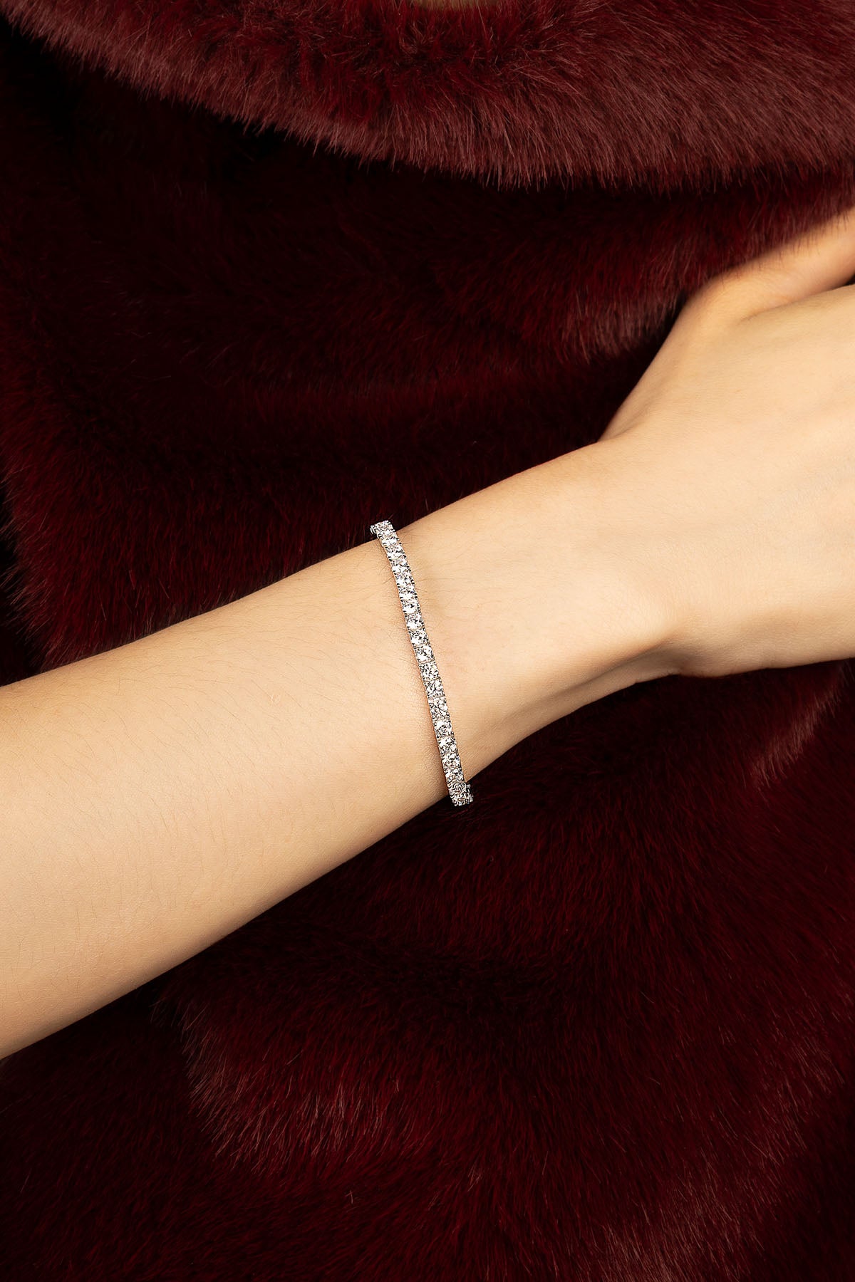 Femme portant le bracelet APM, éclat scintillant sur fourrure bordeaux, élégance intemporelle.