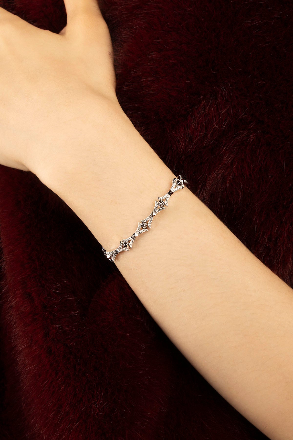 Femme portant le bracelet APM Monaco, une élégance délicate sur fond bordeaux.