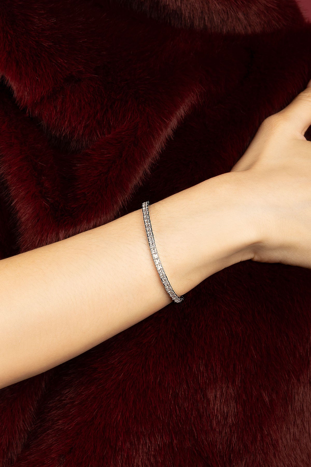 Femme portant le bracelet tennis APM Monaco, éclat scintillant sur velours bordeaux.