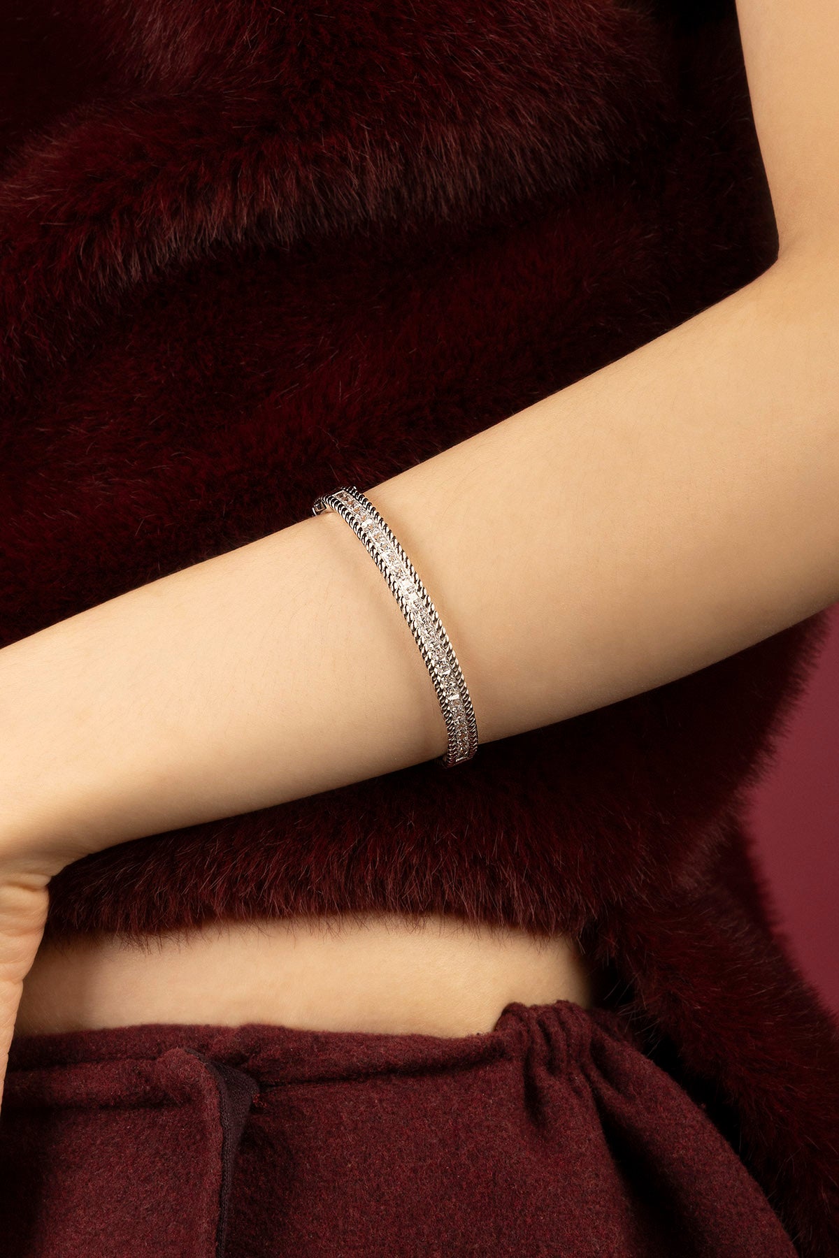 Femme portant un bracelet APM, éclat délicat sur une élégance bordeaux feutrée.