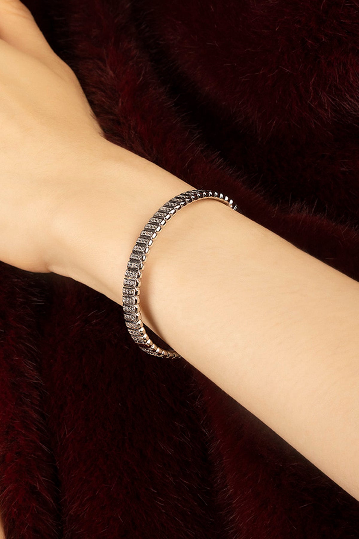 Femme portant le Bracelet APM, éclat scintillant posé sur une douceur bordeaux.