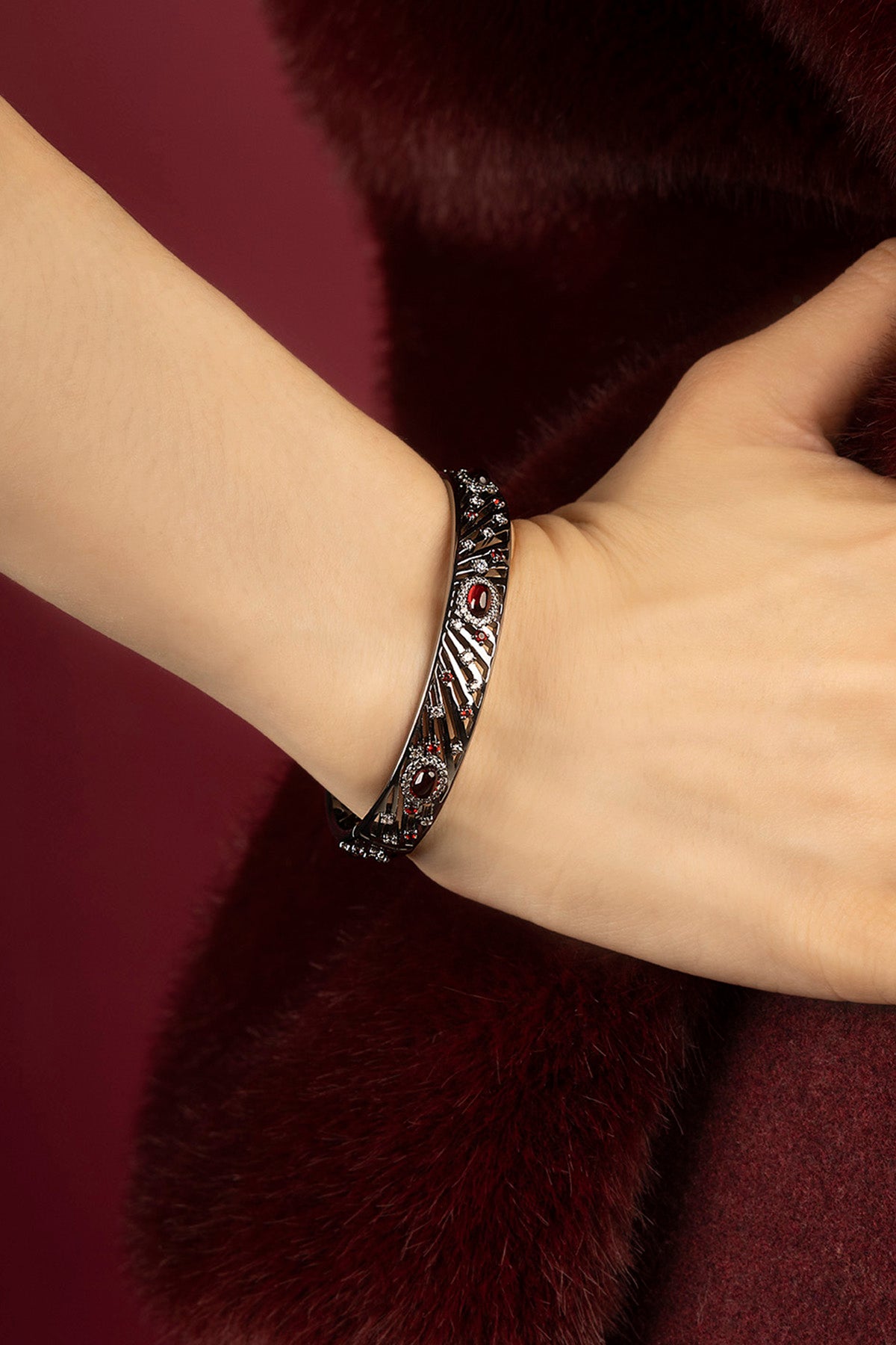 Femme portant le bracelet APM, éclat rubis sur fourrure bordeaux, allure envoûtante.
