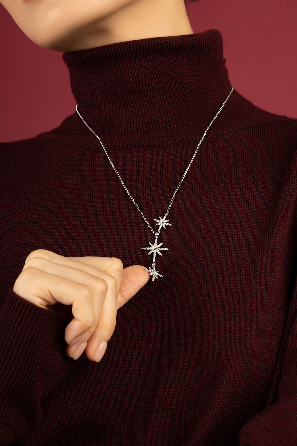 Woman wearing APM Monaco necklace, une pluie d'étoiles scintillantes sur bordeaux profond.