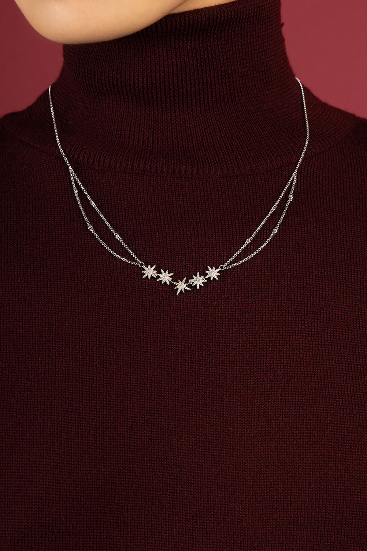 Woman wearing APM collier étoilé, une constellation délicate sur col bordeaux.