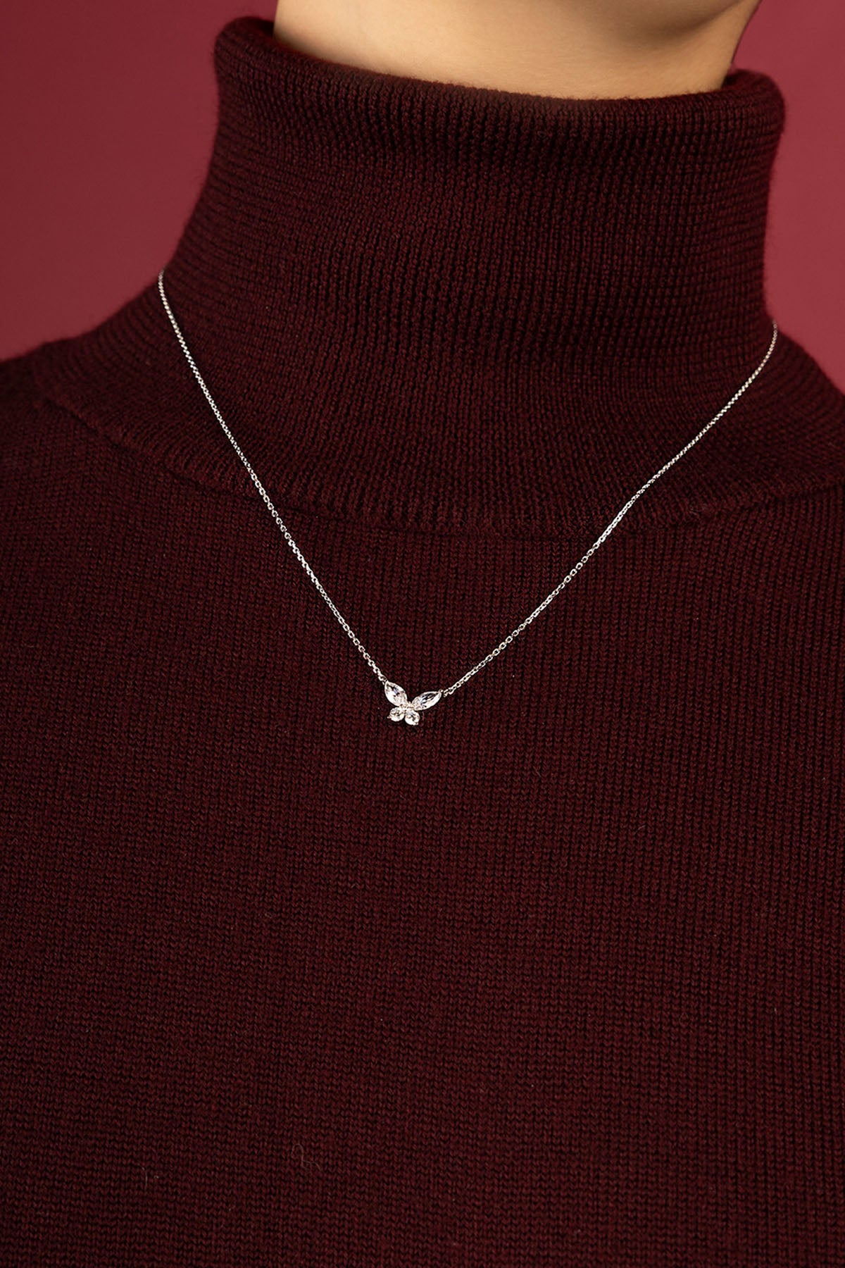 Femme portant le collier papillon APM Monaco, une touche délicate sur maille bordeaux.