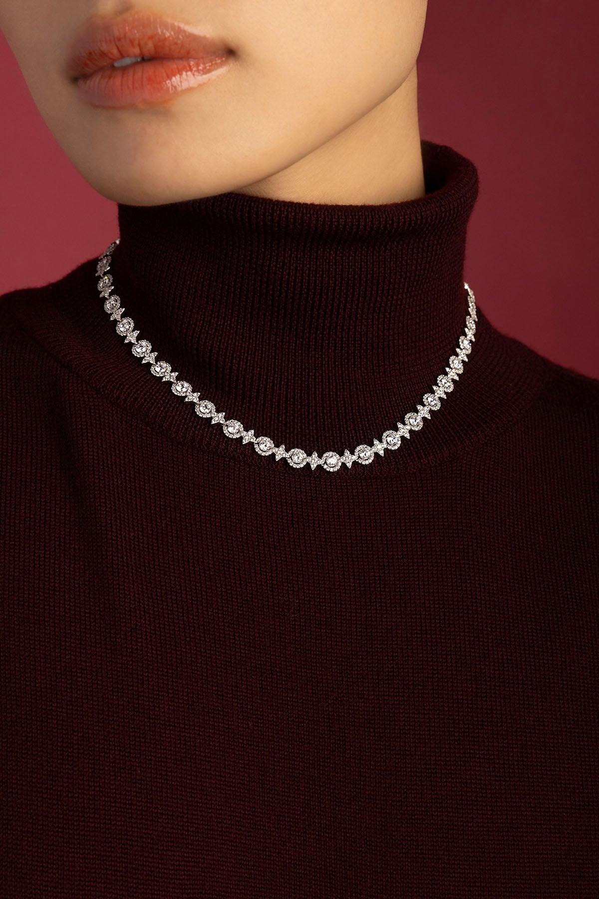 Femme portant le collier APM Monaco, éclat scintillant sur un col bordeaux intemporel.