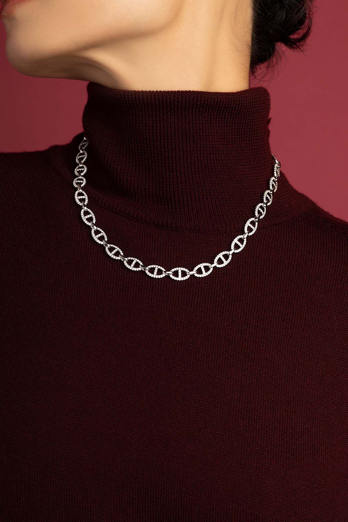 Femme portant le collier APM, éclat lumineux sur bordeaux, allure moderne et raffinée.
