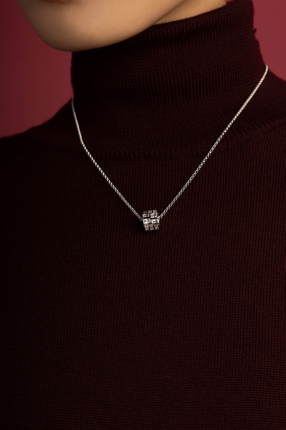 Femme portant le collier APM, éclat cubique sur col roulé bordeaux, élégance discrète et moderne.