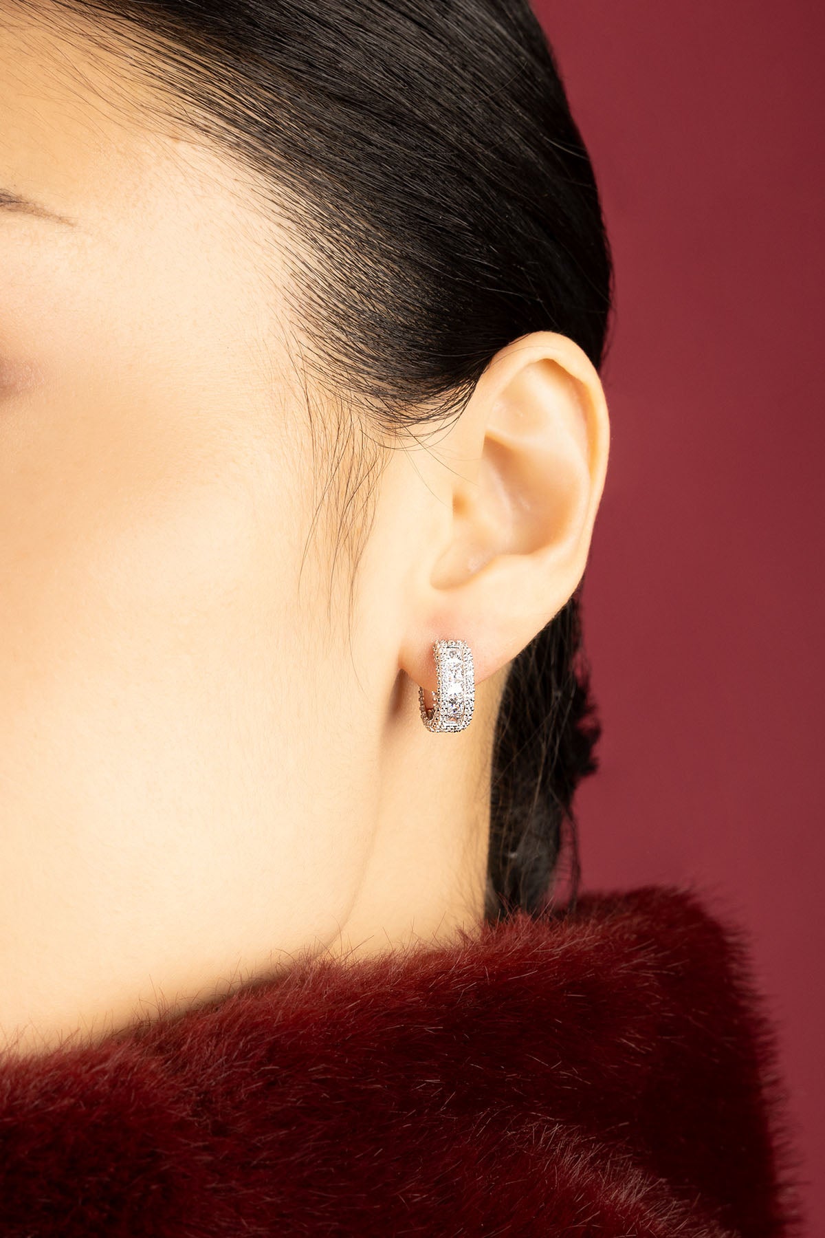 Woman wearing APM hoop earrings, éclat scintillant sur velours bordeaux.