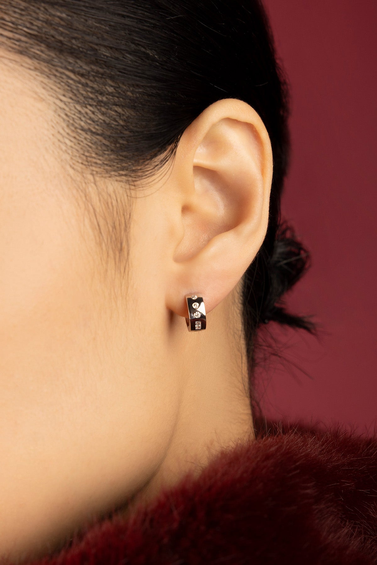Femme portant les APM boucles d'oreilles, une élégance discrète sur fond bordeaux.