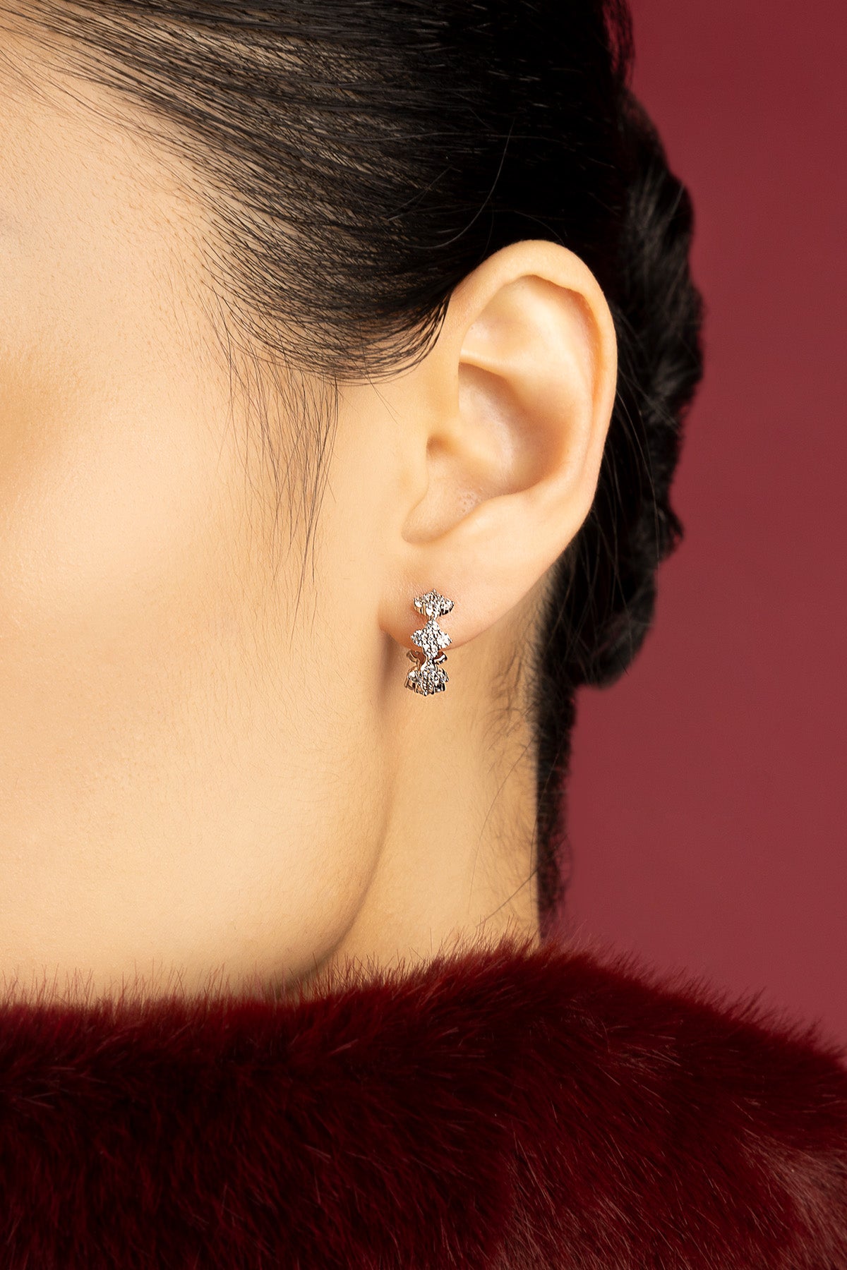 Femme portant les boucles d'oreilles APM, éclat scintillant sur fond bordeaux envoûtant.