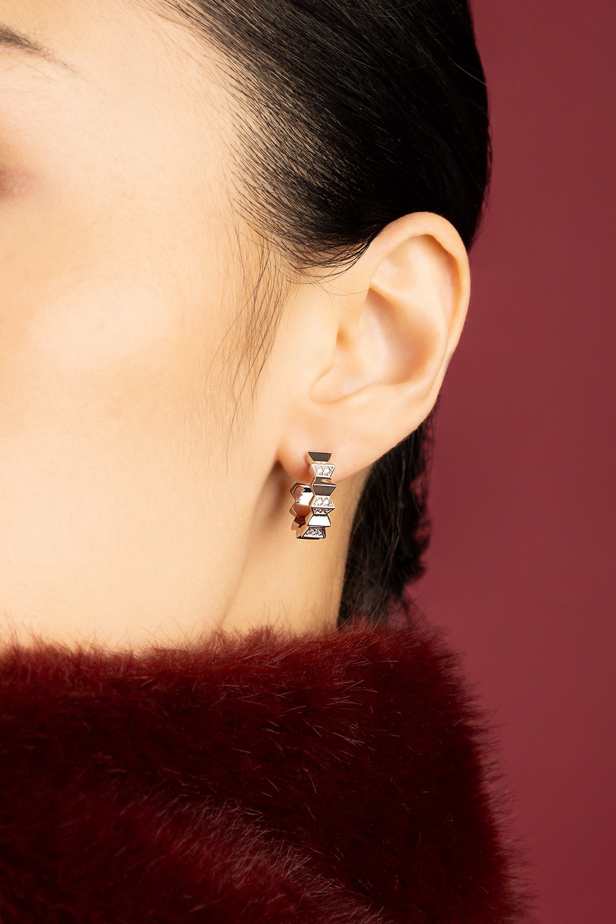 Woman wearing APM Monaco boucles d'oreilles géométriques, éclat sculpté sur fourrure bordeaux.