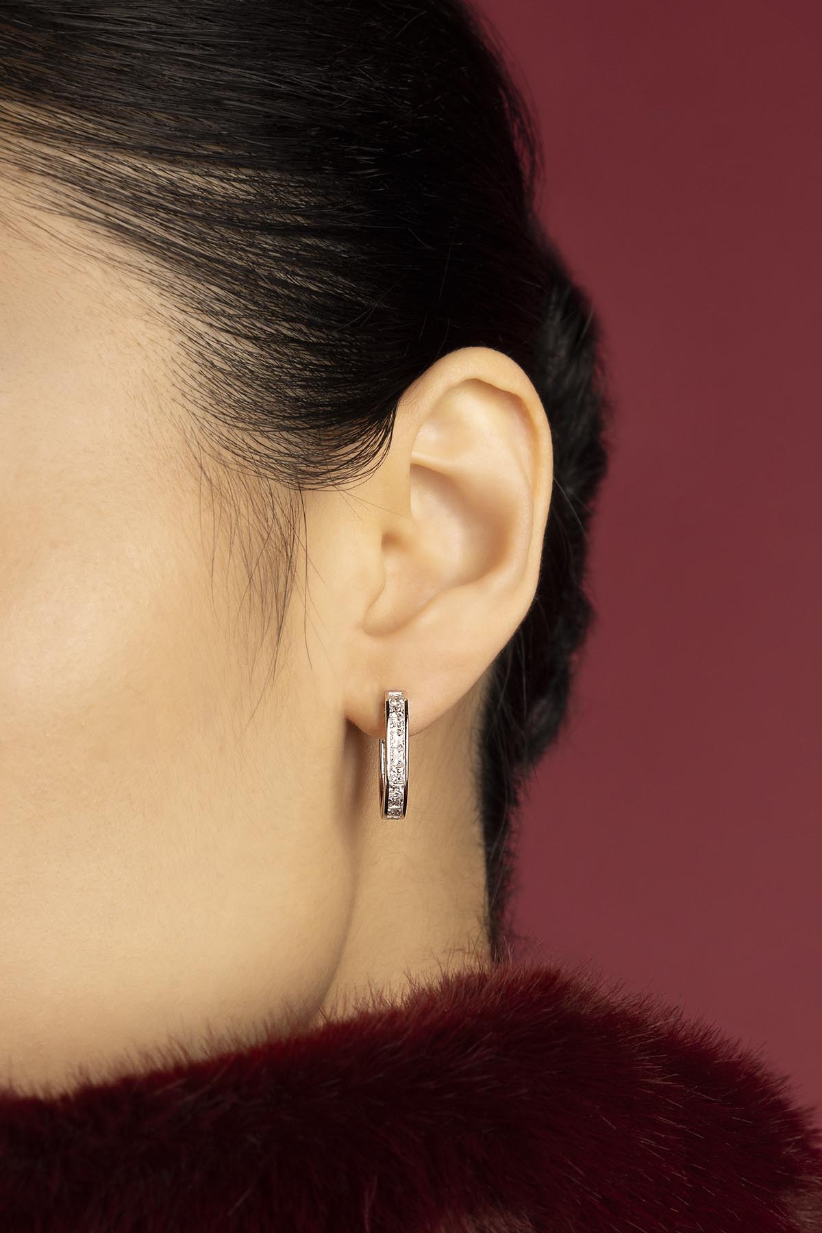 Femme portant les boucles d'oreilles APM, éclat délicat sur fond bordeaux envoûtant.