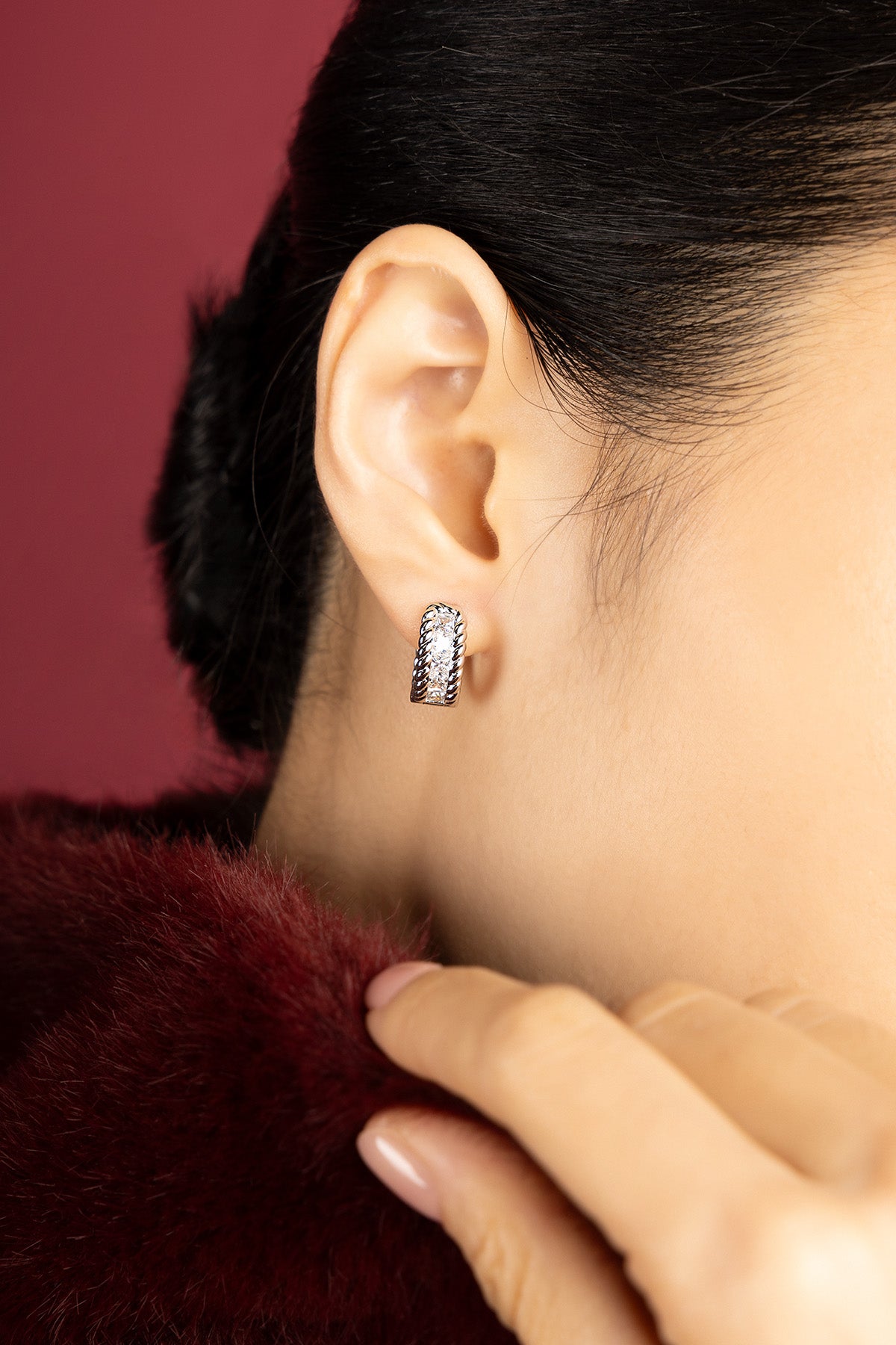 Femme portant les Boucles d'Oreilles APM Monaco, éclat torsadé et allure sophistiquée sur fourrure bordeaux.