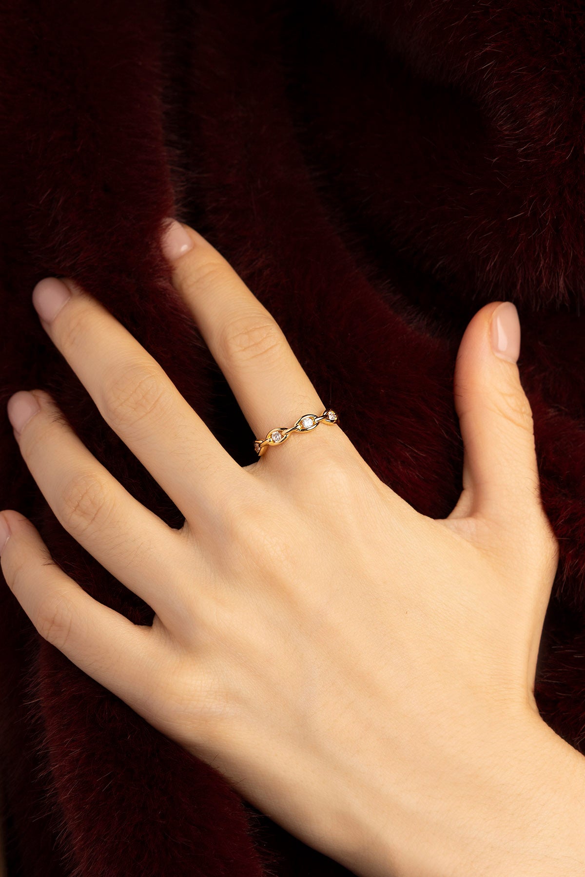 Femme portant la Bague APM Monaco, une élégance dorée délicatement lumineuse sur fourrure bordeaux.