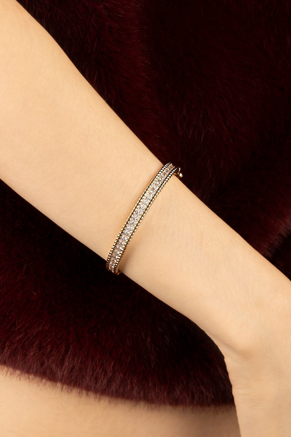 Femme portant le bracelet APM doré scintillant, une élégance chaleureuse sur fourrure bordeaux.