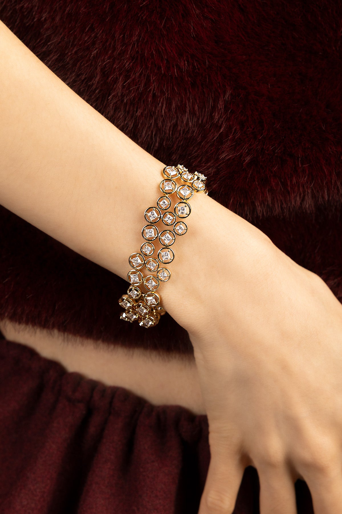 Femme portant le bracelet APM, éclat doré et scintillement délicat sur fond bordeaux.