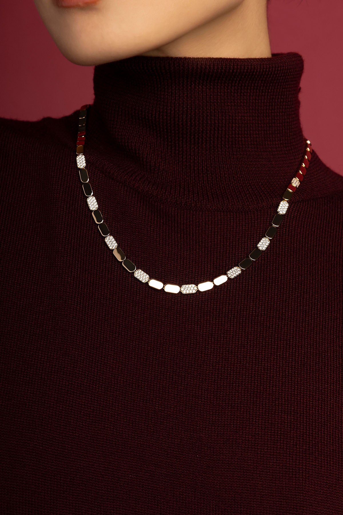 Woman wearing APM necklace, éclat doré et scintillant sur bordeaux profond.