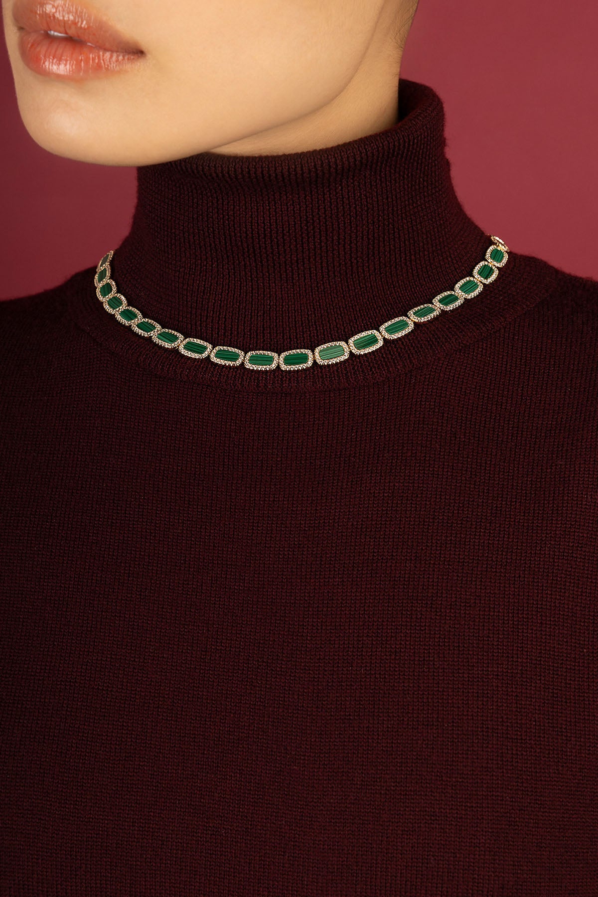 Femme portant le collier APM, éclat vert profond sur bordeaux, allure raffinée et intemporelle.