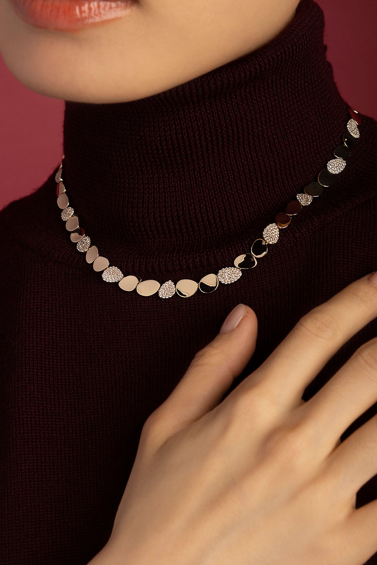 Femme portant le collier APM Monaco, une élégance lumineuse posée sur un col bordeaux.