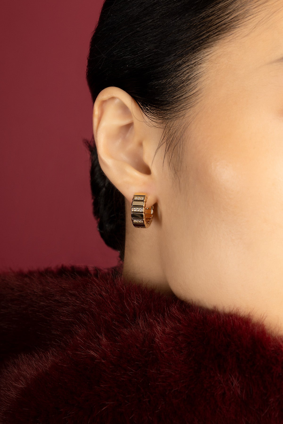 Femme portant les Boucles d'Oreilles APM, une allure dorée et sculpturale sur fourrure bordeaux.