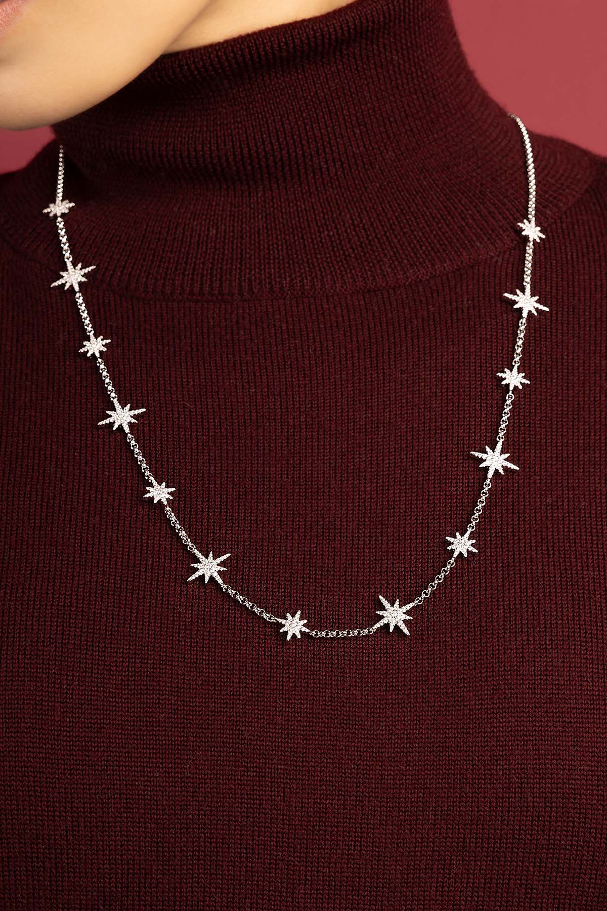 Femme portant un collier APM Monaco étoilé, éclat céleste sur bordeaux profond.