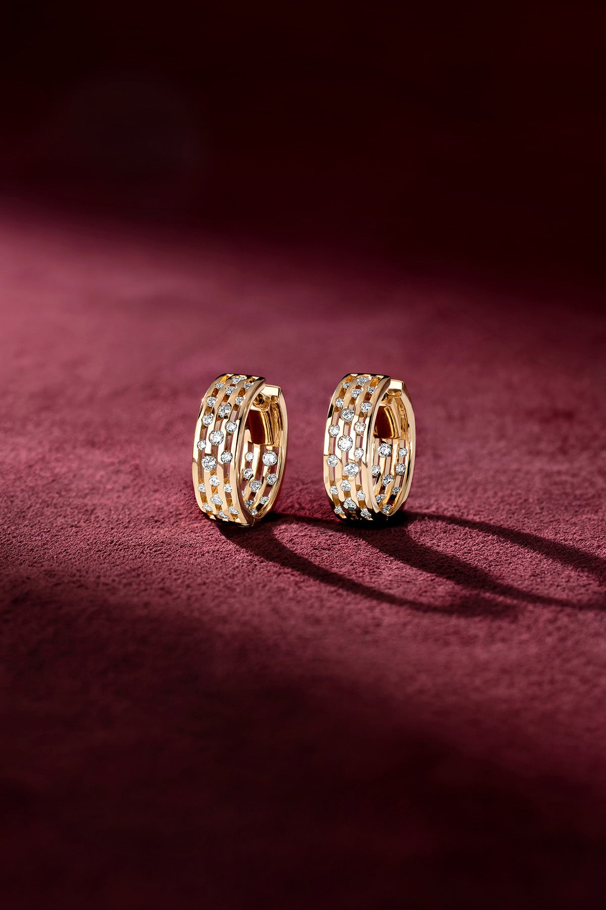 Boucles d'oreilles APM Monaco, éclat doré et scintillant sur velours grenat.