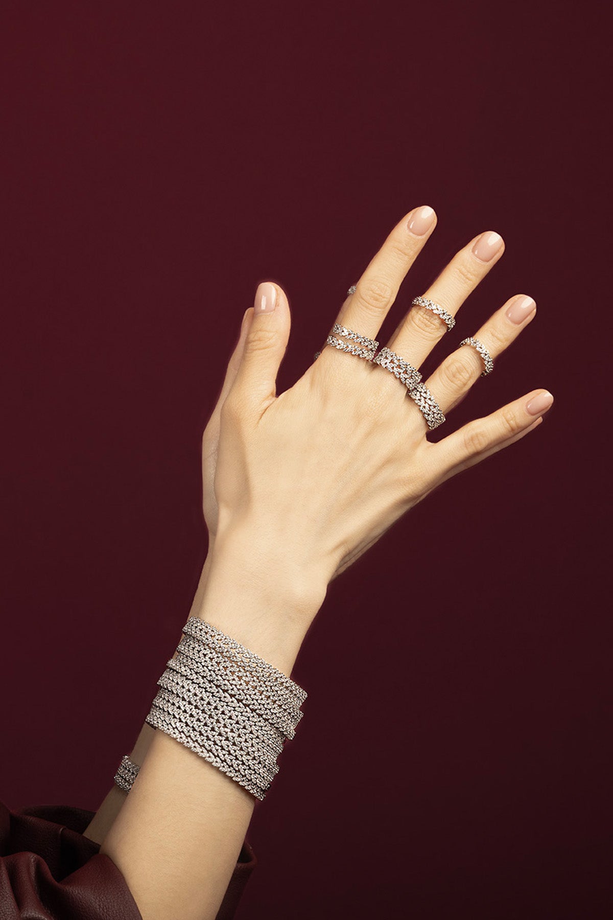 Femme portant les bracelets et bagues APM Monaco, éclat scintillant sur fond bordeaux profond.