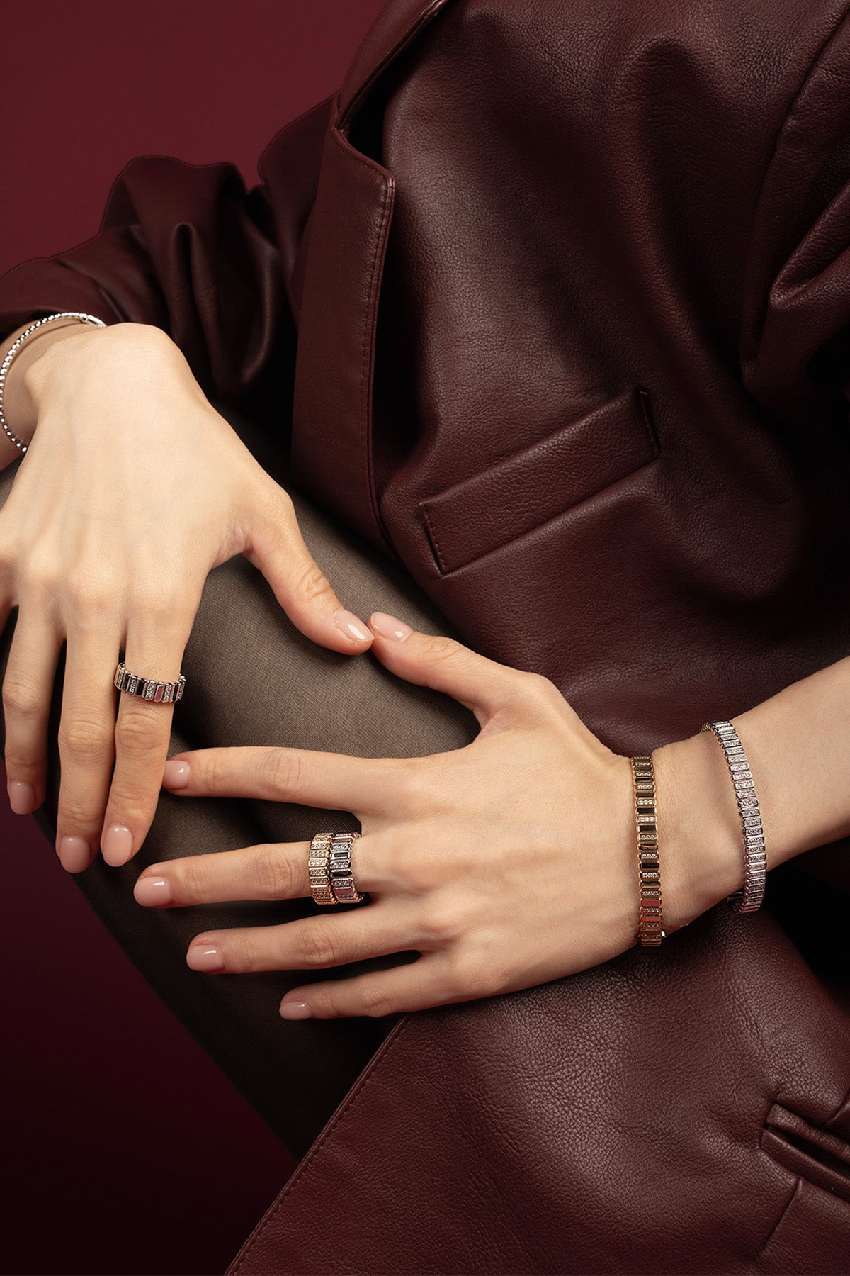 Femme portant les bagues et bracelets APM Monaco, éclat contemporain sur cuir bordeaux.