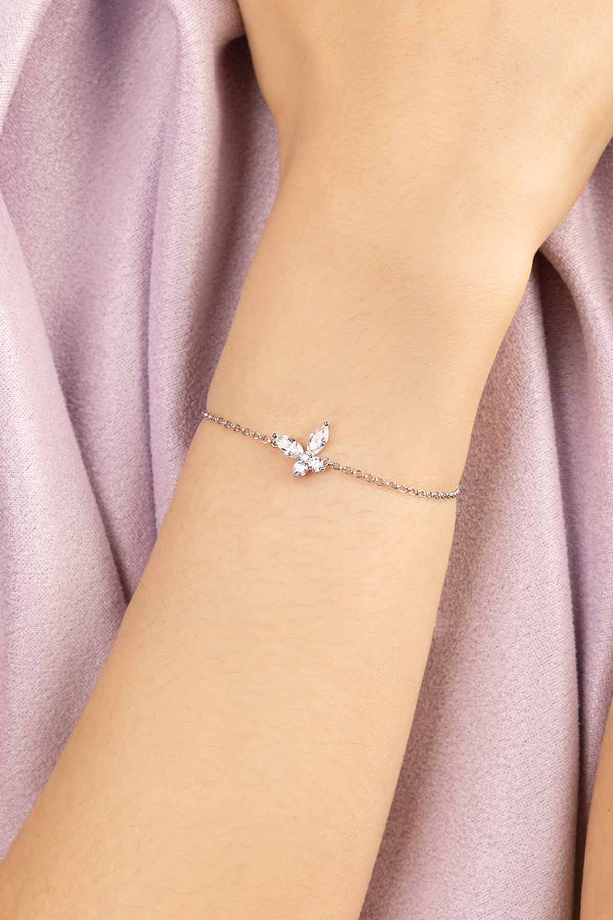 Silver bracelet with a butterflyshaped clasp on a wrist against a soft pink fabric background
