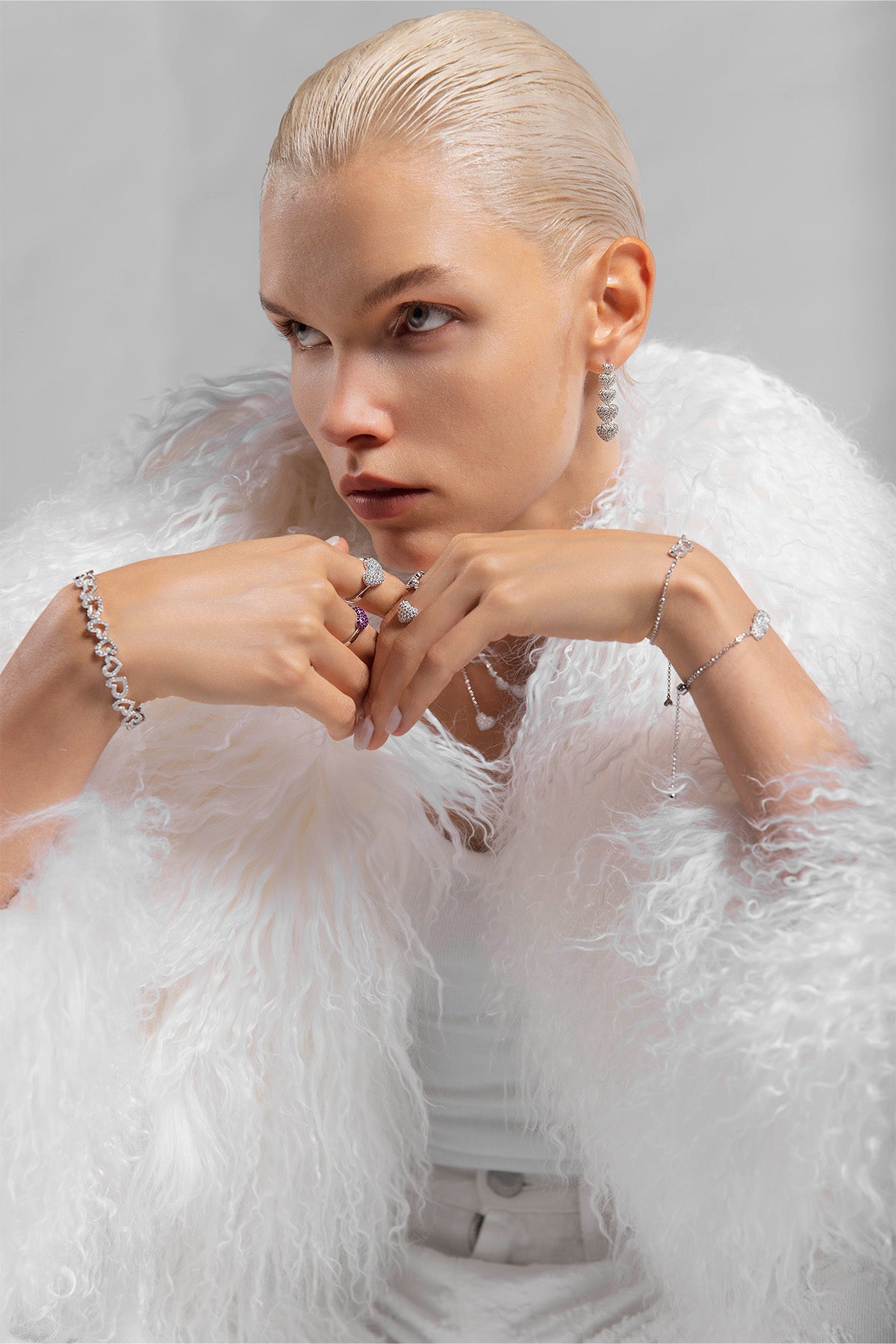 Woman with APM MONACO jewelry and wearing a white feathered coat against a gray background