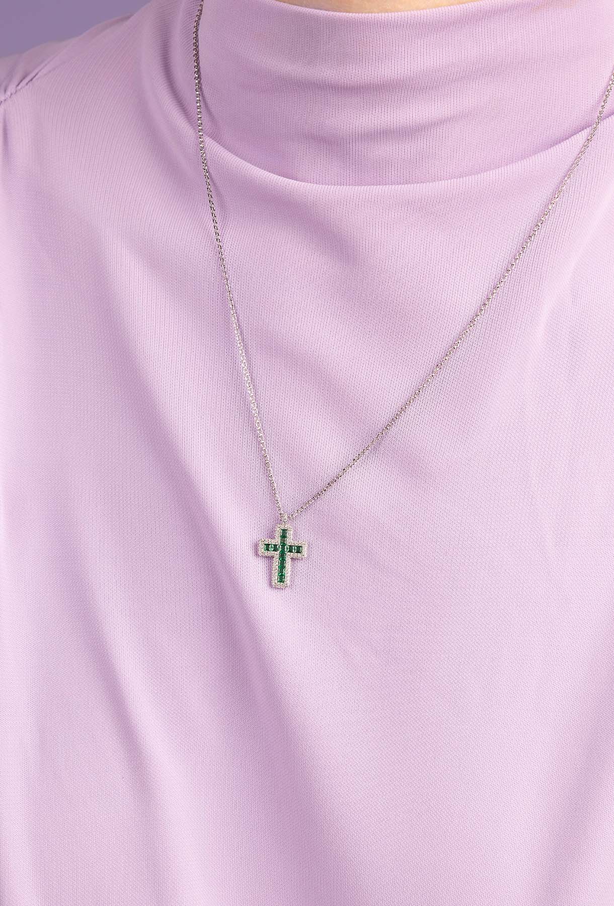 APM MONACO silver necklace with a green cross pendant on a light purple background