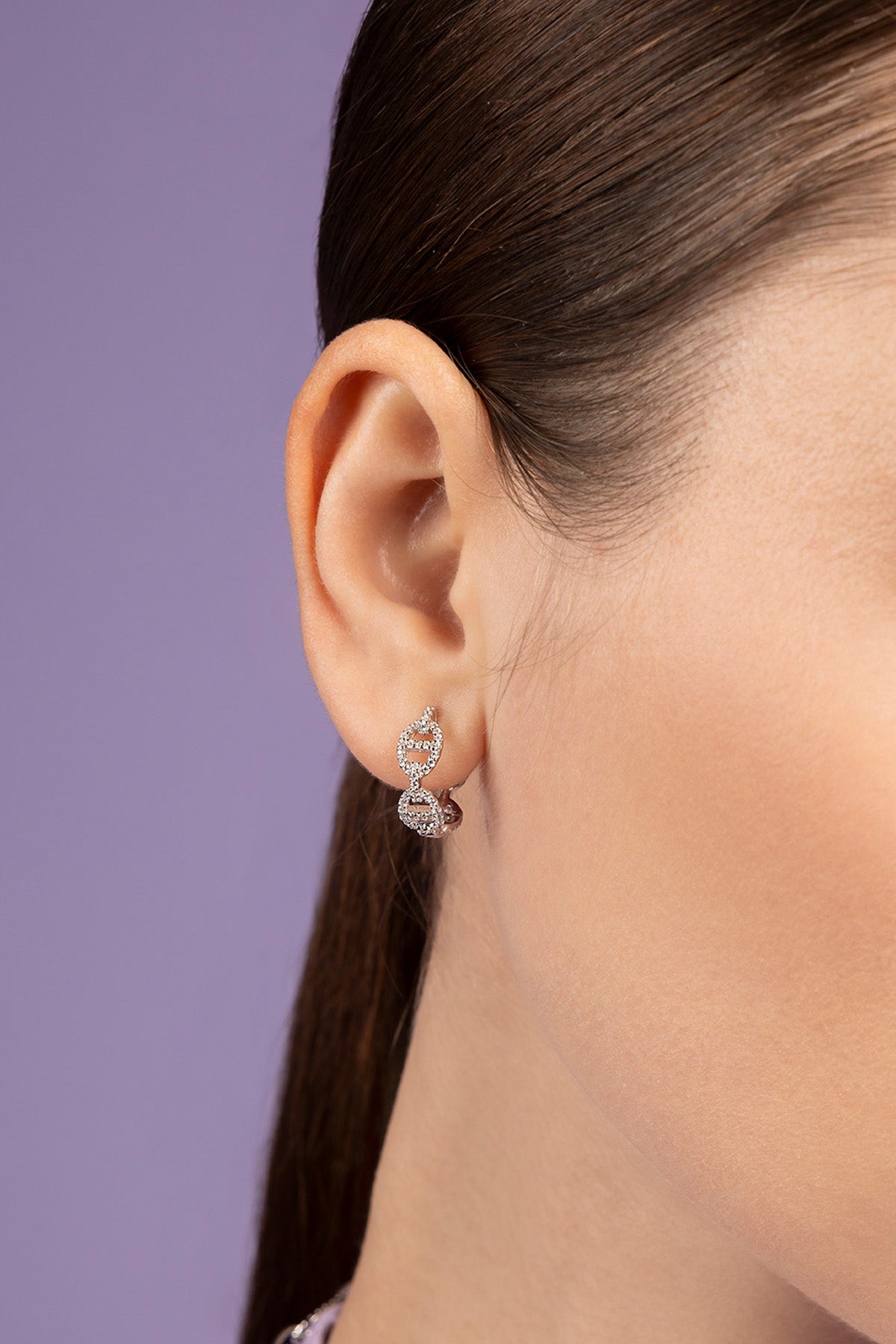 Close-up of an ear wearing a diamond earring with dark hair and skin background
