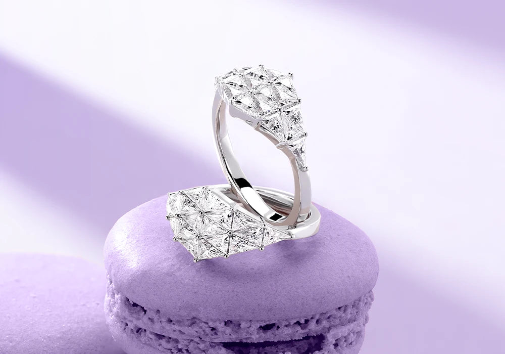 APM MONACO geometric rings with white stones on a purple macaron against a light purple background.