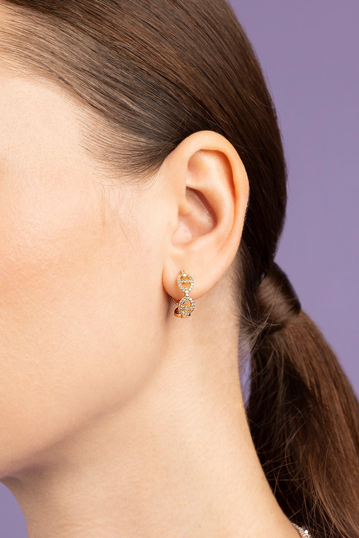 Close-up of an ear wearing a gold earring with a dark background