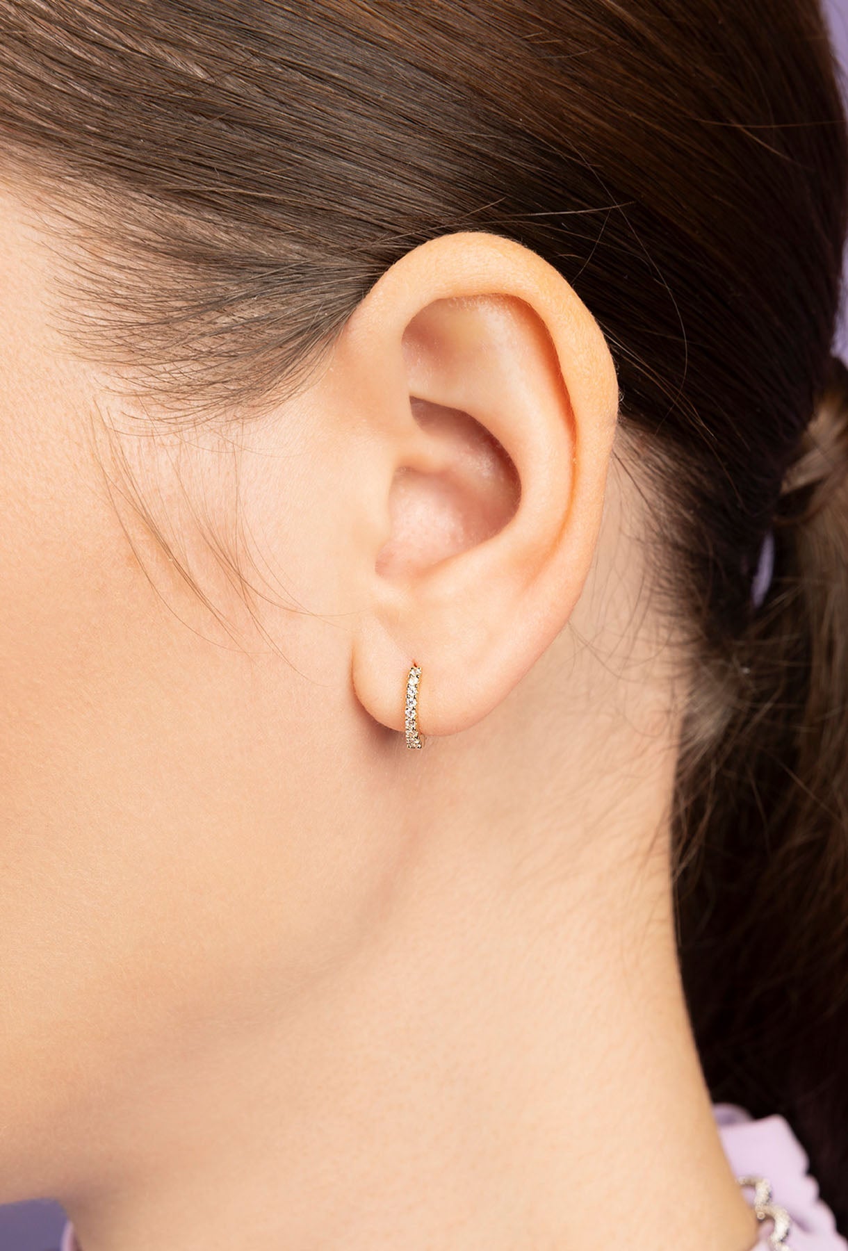 Close-up of a person wearing a huggie earring from APM MONACO with a soft gray background